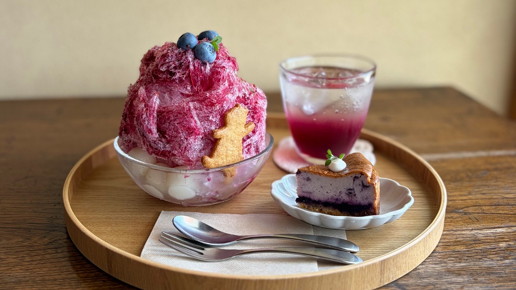 くまのクッキーがのったかき氷とチーズケーキとドリンクが丸盆にのっている